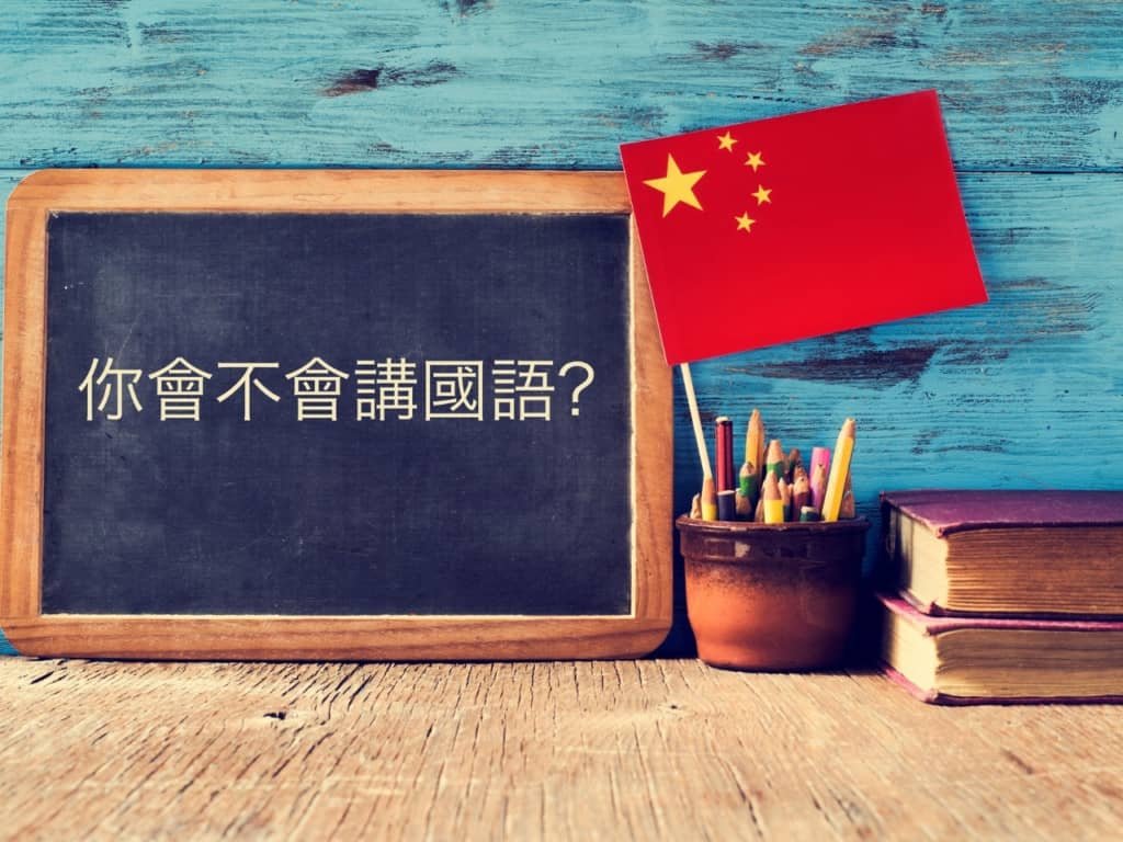 Fotografía de una bandera China junto a un tablero con caracteres chinos escritos.